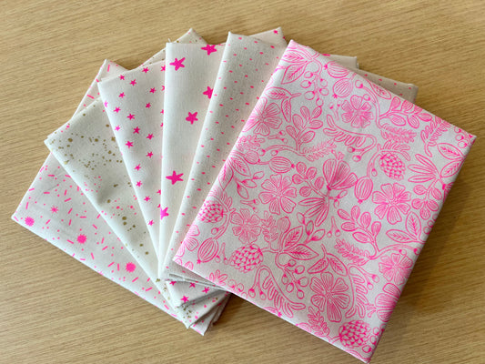 Set of fabric samples with neon pink floral and star patterns on a wooden surface