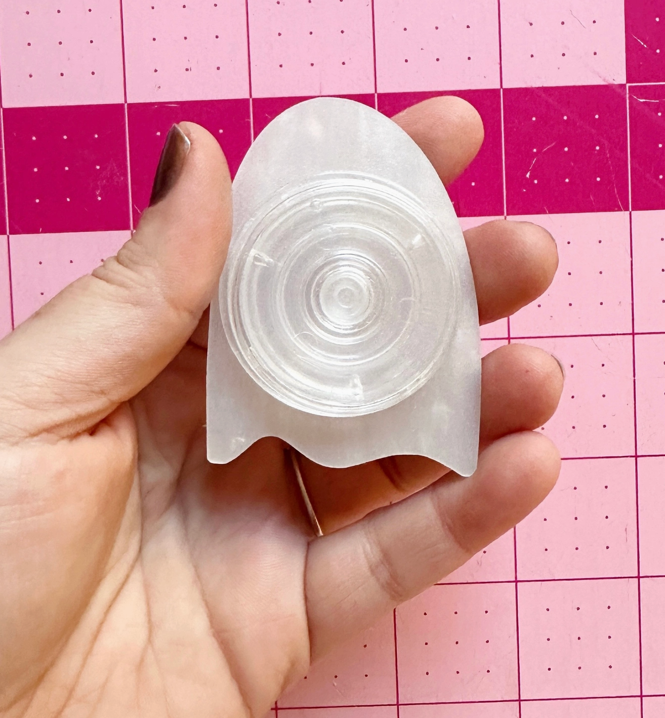 Clear silicone mold held in a hand against a pink grid background