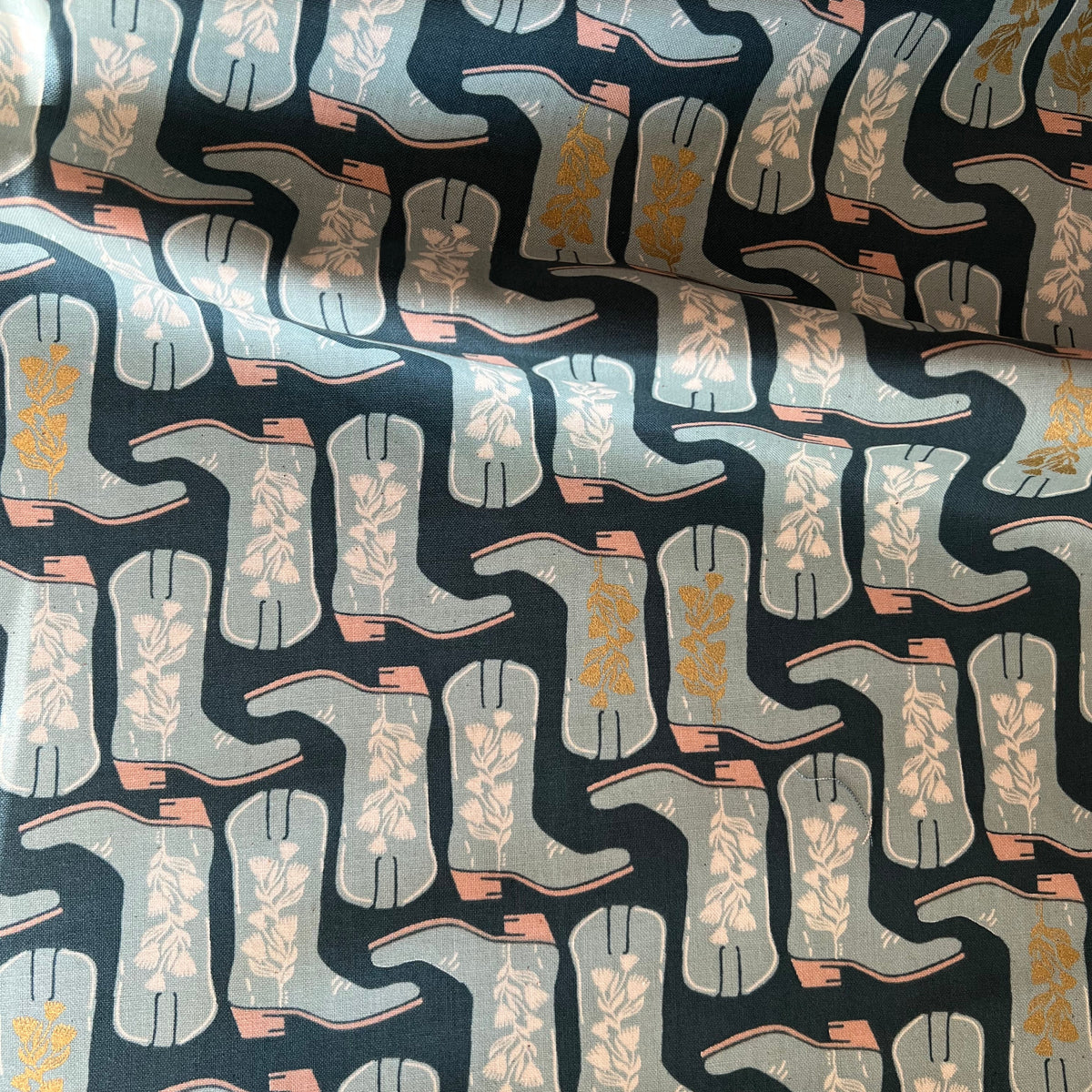 A piece of fabric with a geometric pattern featuring cowboy boots in a variety of shades of blue and metallic accents.